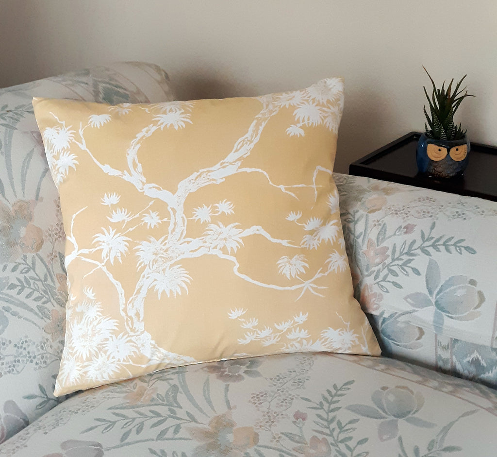 Handmade 18x18 Chinoiserie bonsai pine throw pillow cover in white on warm golden yellow polished cotton, styled on a bed